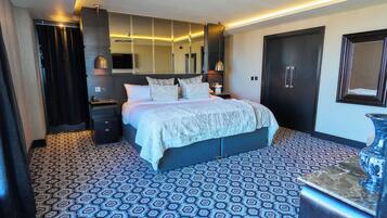 Una habitación de hotel moderna con una cama grande, un armario de madera oscura, una mesita de noche y un espejo amplio.