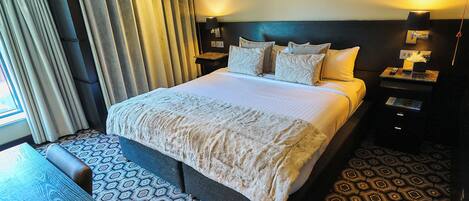 A hotel room with a large bed, a bedside table, a lamp, and a patterned carpet.
