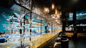 A bar area with a long counter, multiple glasses, and shelves stocked with bottles. - The Vincent Hotel (Southport)