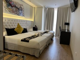 Une chambre d’hôtel avec un grand lit, deux petits lits, un bureau et une télévision.