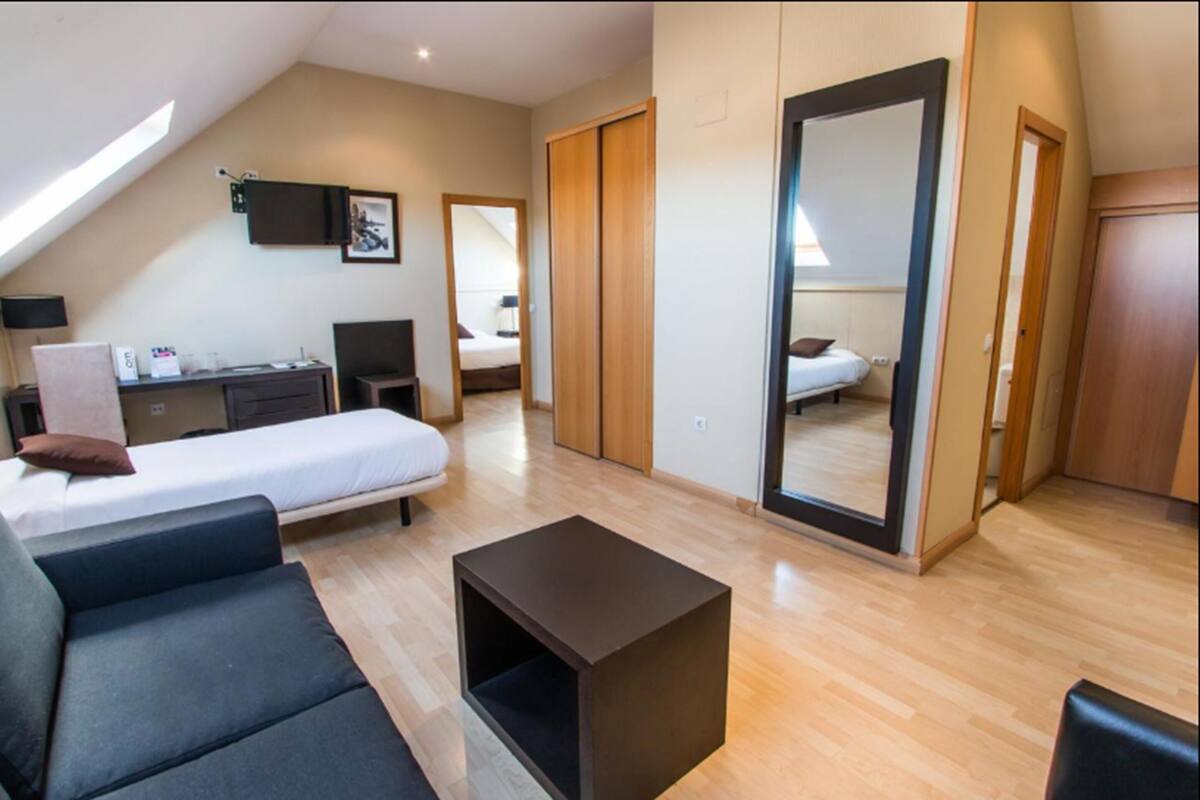 Habitación de hotel moderna con cama tipo altillo, un sofá, una mesita y un espejo grande.
