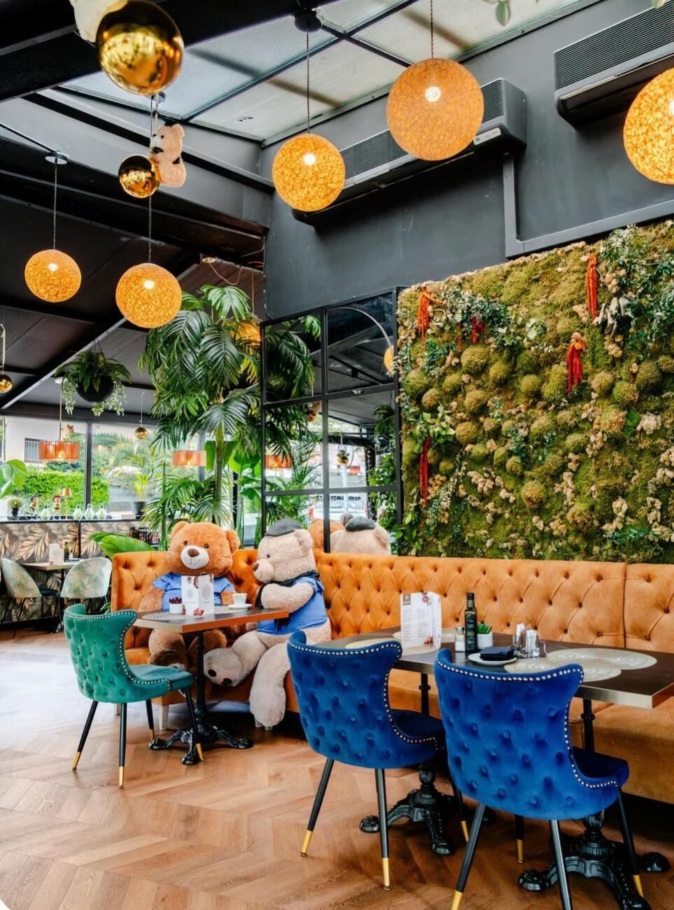 A restaurant interior with a green wall, plush seating, and hanging spherical lights.