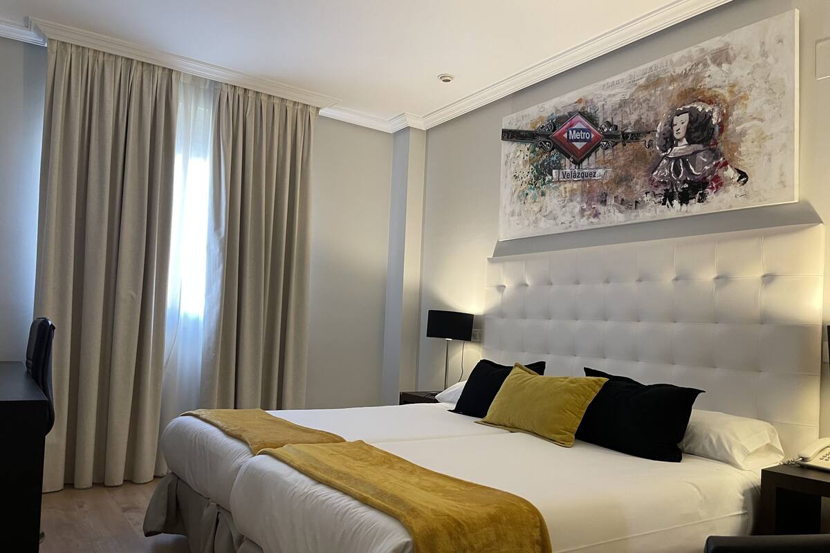 Una habitación de hotel con una cama grande, cabecera, un cuadro sobre la cama, un escritorio y una silla.
