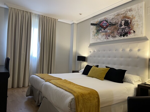 Una habitación de hotel con una cama grande, cabecera, un cuadro sobre la cama, un escritorio y una silla.