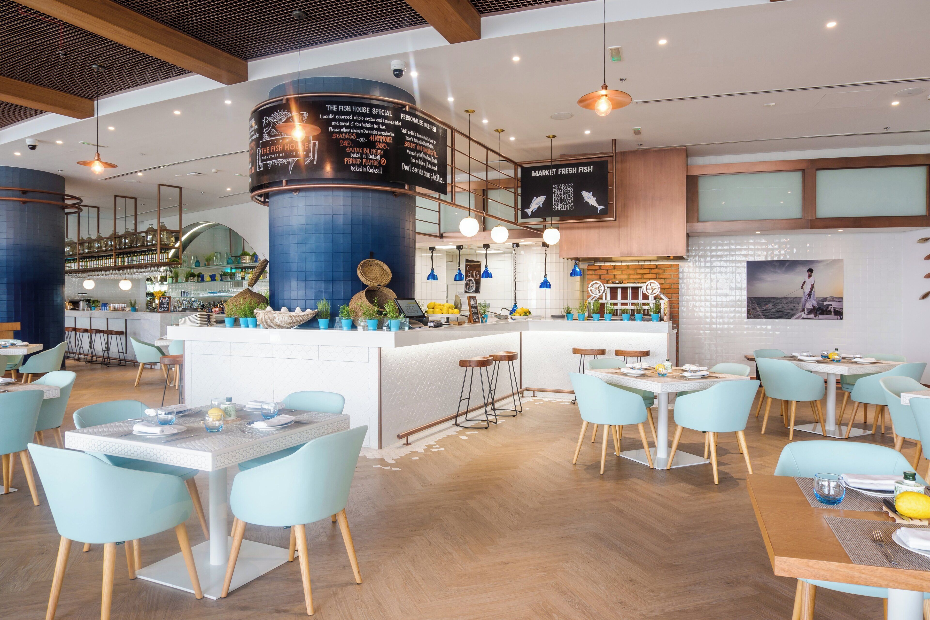 En modern restaurang med en central bardisk, flera olika typer av sittplatser och en väl synlig meny.