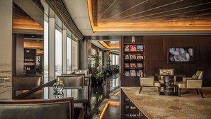 Een moderne hotellobby met een glazen salontafel, lederen fauteuils, een boekenkast en een televisie aan de muur.