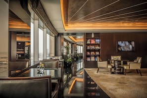 En moderne hotellobby med et glasbord, læderstole, en bogreol og et fjernsyn på væggen.