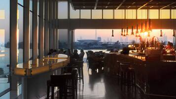 A bar with a view of a city skyline at sunset, large windows, and modern interior design.
