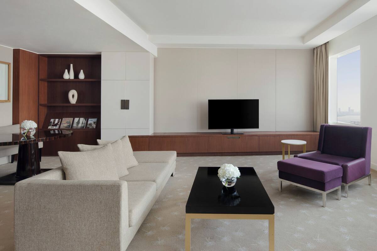 Una sala de estar moderna con un sofá, una mesa de centro, un sillón morado, un televisor y una estantería.