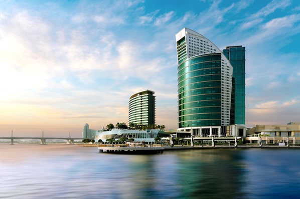 A modern hotel with a curved facade, located near a waterfront with a bridge in the background. - InterContinental Dubai Festival City by IHG (Dubai)