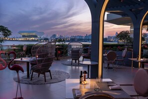 An outdoor dining area with round tables and wicker chairs, overlooking a city skyline and a body of water. - InterContinental Dubai Festival City by IHG (Dubai)