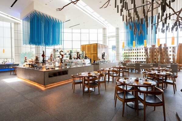 Un restaurante moderno con una zona de bar central, varias mesas y sillas para comer.
