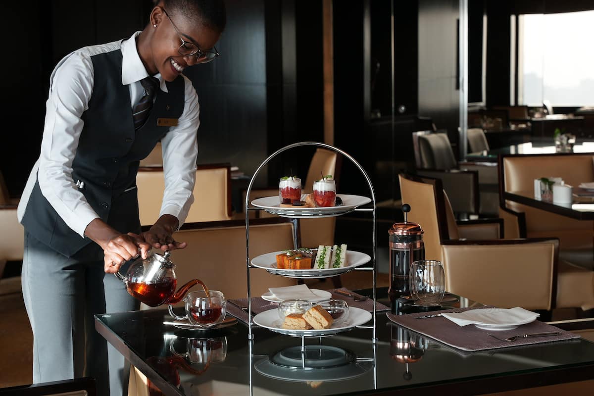 Zona de comedor de hotel con un soporte de postres de tres niveles, un servicio de té y una mesa preparada para una comida.