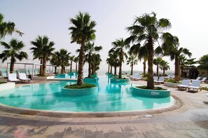 Ein Poolbereich mit Palmen, Liegestühlen und blauem Himmel.