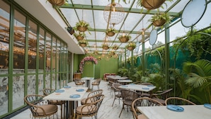 A restaurant with a greenhouse interior, featuring tables and chairs, hanging planters, and a green wall with a floral wreath. - Royal Orchid Central Jaipur (Jaipur)
