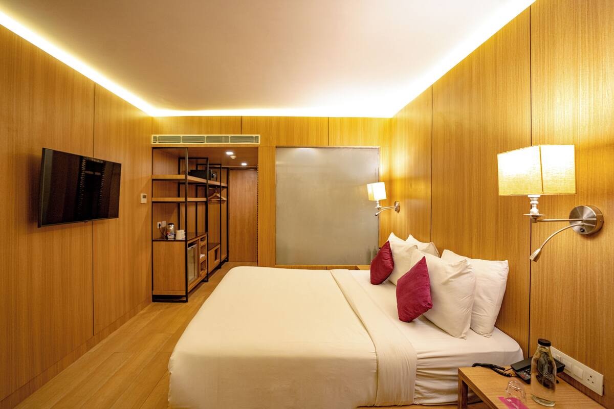 Una habitación de hotel con una cama grande, paredes de madera, un televisor, un armario y una mesita de noche con una lámpara.
