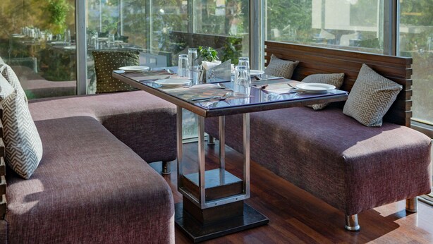 A modern dining area with a glass table, cushioned seating, and a hanging light fixture. - Royal Orchid Central Jaipur (Jaipur)