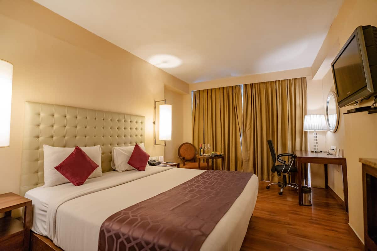 Una habitación de hotel con una cama grande, un escritorio, una silla, un televisor y una lámpara.