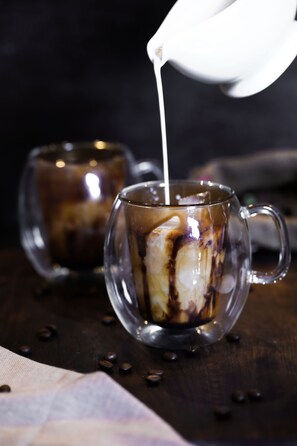 Duas chávenas de vidro transparentes com café gelado, uma delas a ser enchida com leite.
