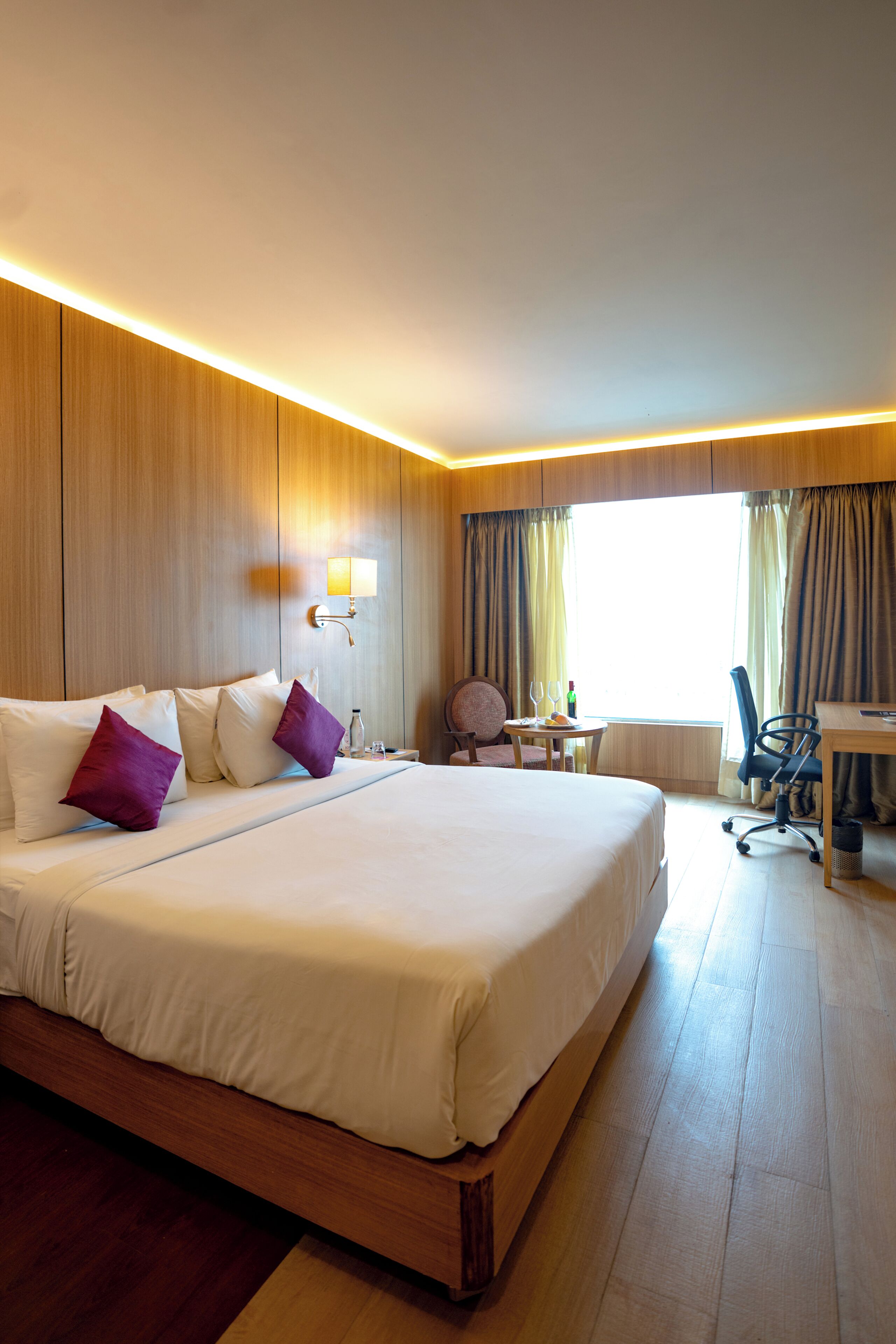 A hotel room with a large bed, a desk, a chair, and a small table.