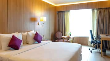 A hotel room with a large bed, a desk, a chair, and a small table.