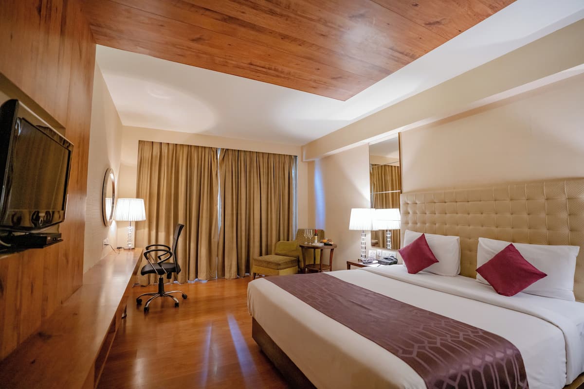 Habitación de hotel con una cama grande, techo de madera, televisor, escritorio con lámpara y una silla.