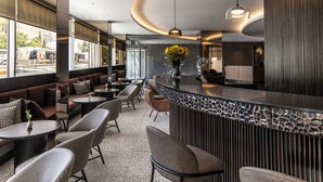 Un espace bar moderne, doté de sièges, d’un comptoir et d’une grande fenêtre donnant sur la rue.