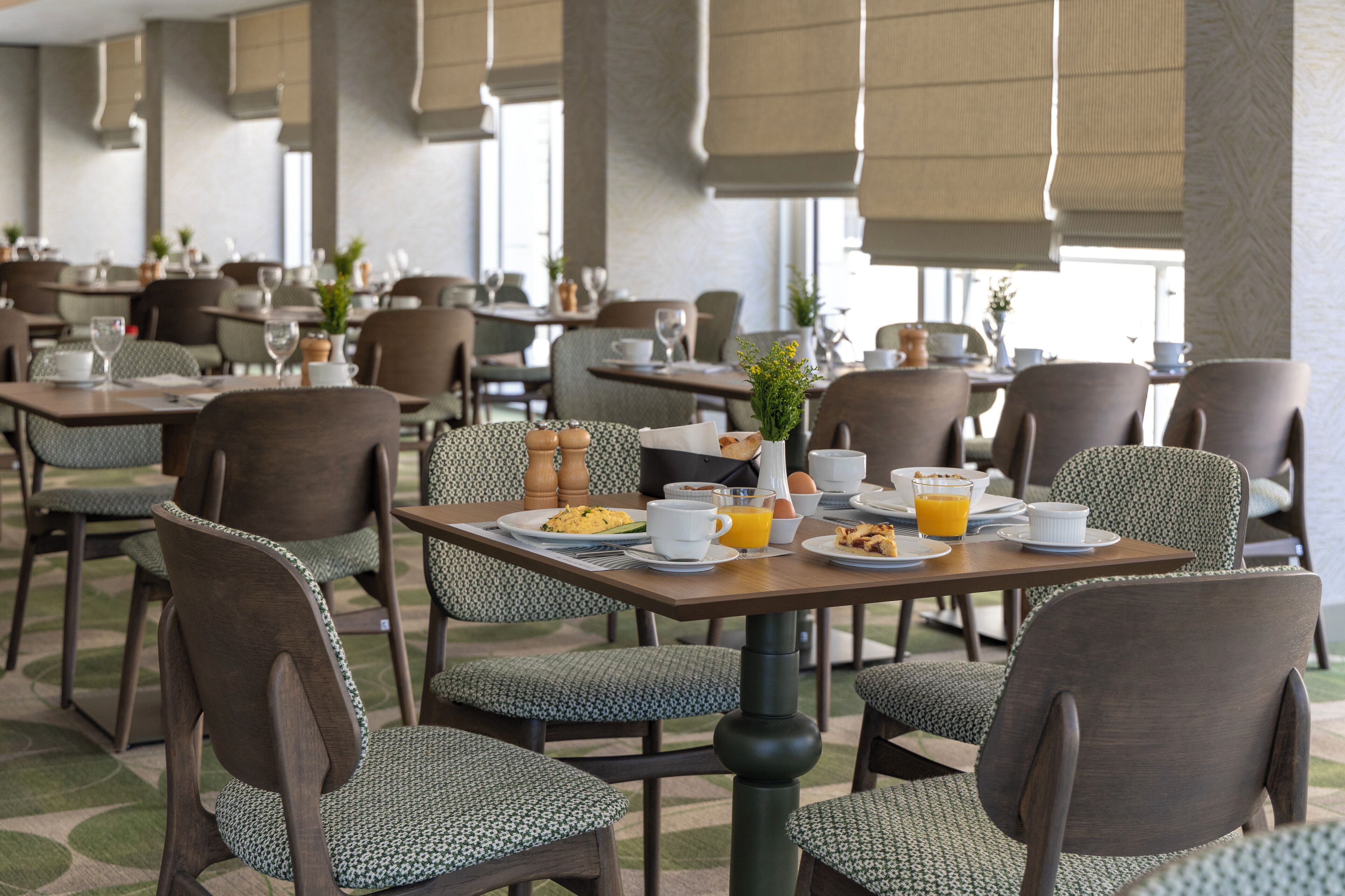 Une salle à manger d’hôtel avec plusieurs tables et chaises, un buffet de petit-déjeuner et une vue sur l’extérieur.