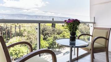 Uma varanda com mesa de vidro, duas cadeiras e um vaso com flores.
