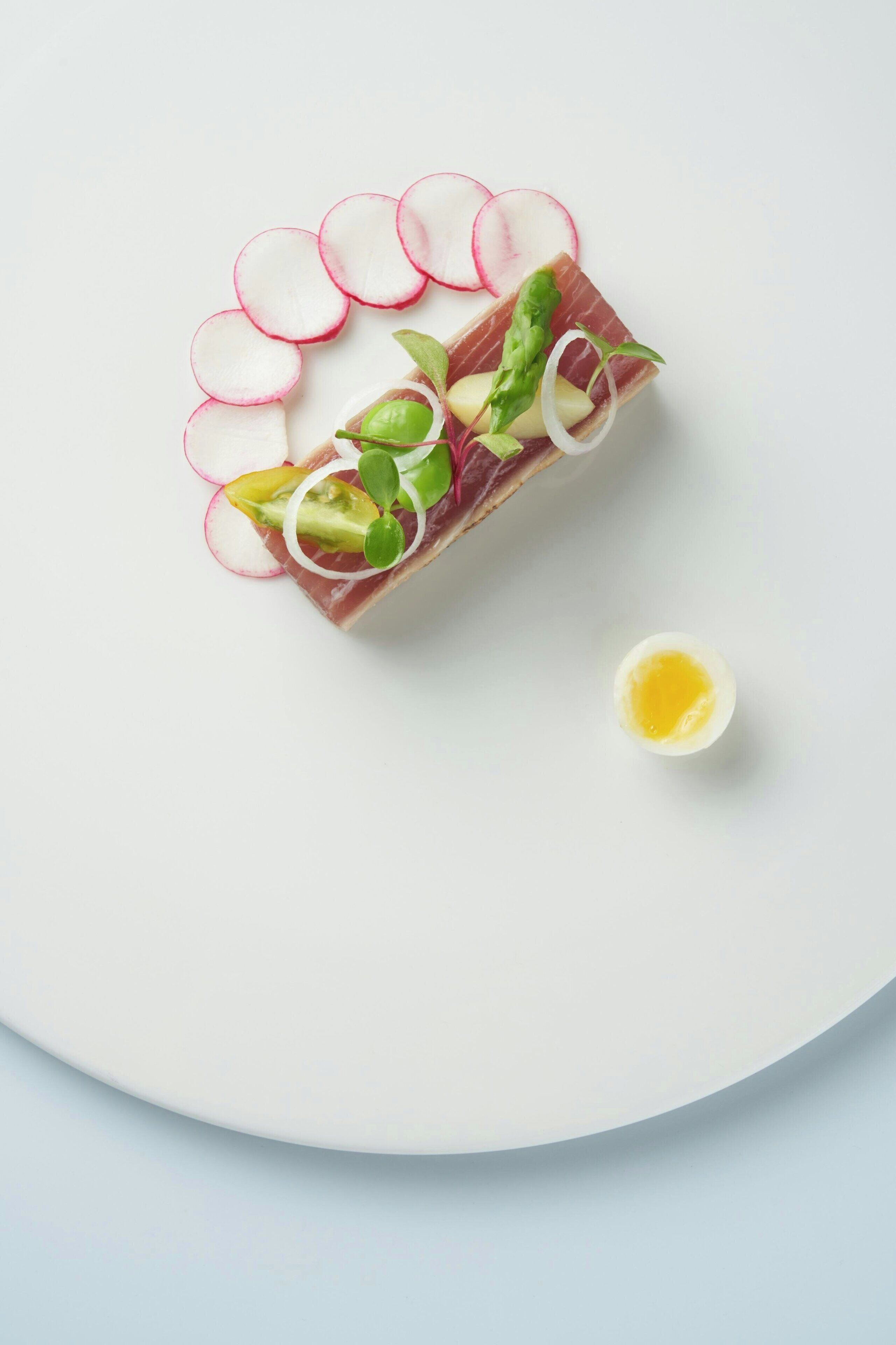A dish with sliced radishes, avocado, and greens on a white plate.