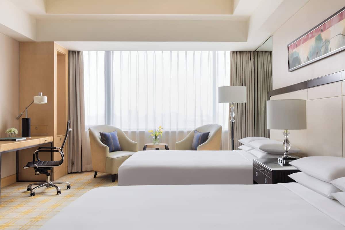A hotel room with two beds, a desk, a chair, and a nightstand with lamps.