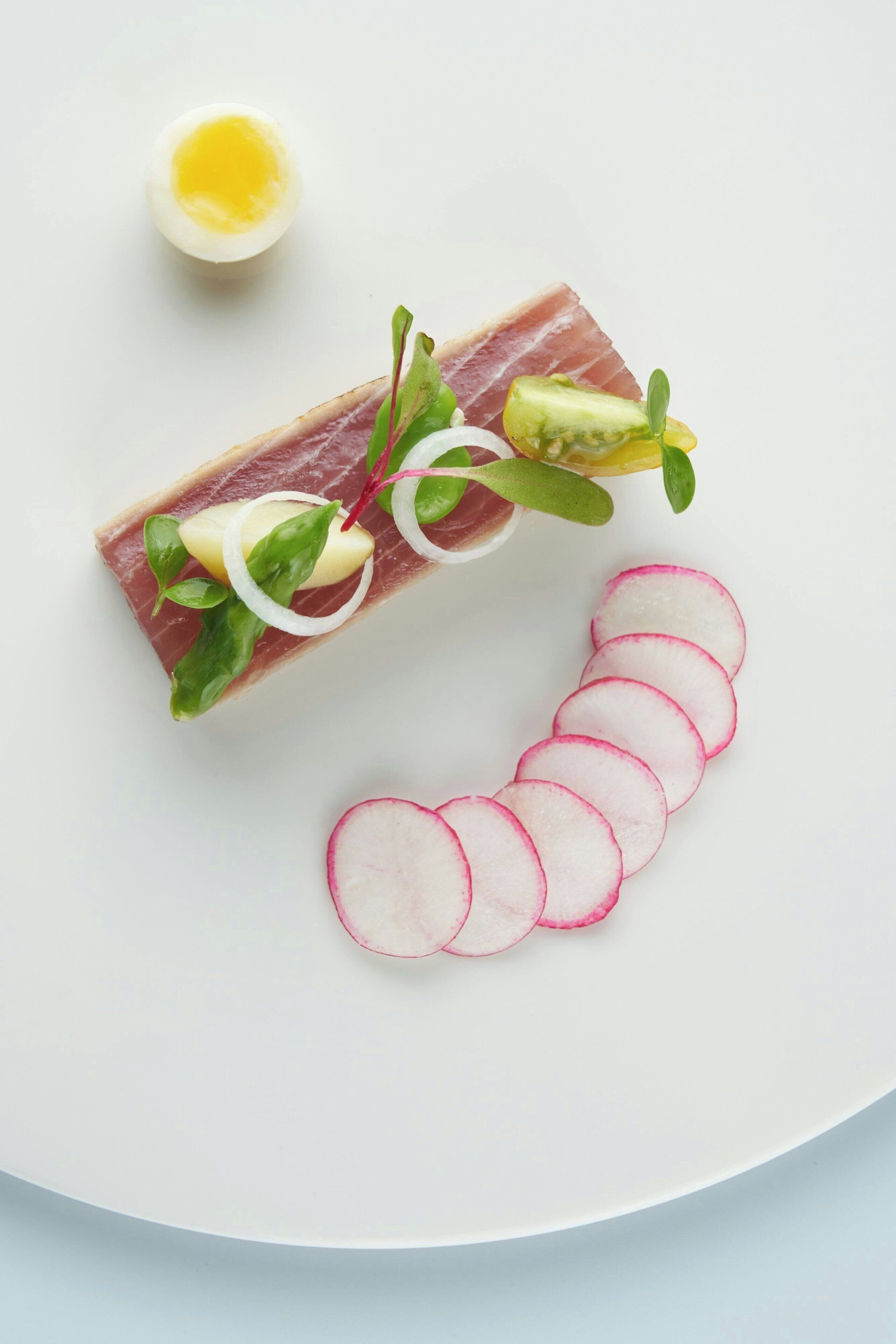 Un plato con una rebanada de carne, rodajas de rábanos, medio huevo duro y algunas verduras.