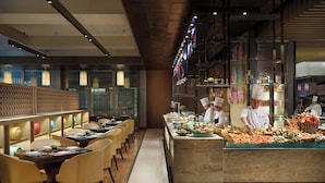 Un restaurante moderno con barra libre, cocineros preparando comida y un área de comedor con mesas y sillas.