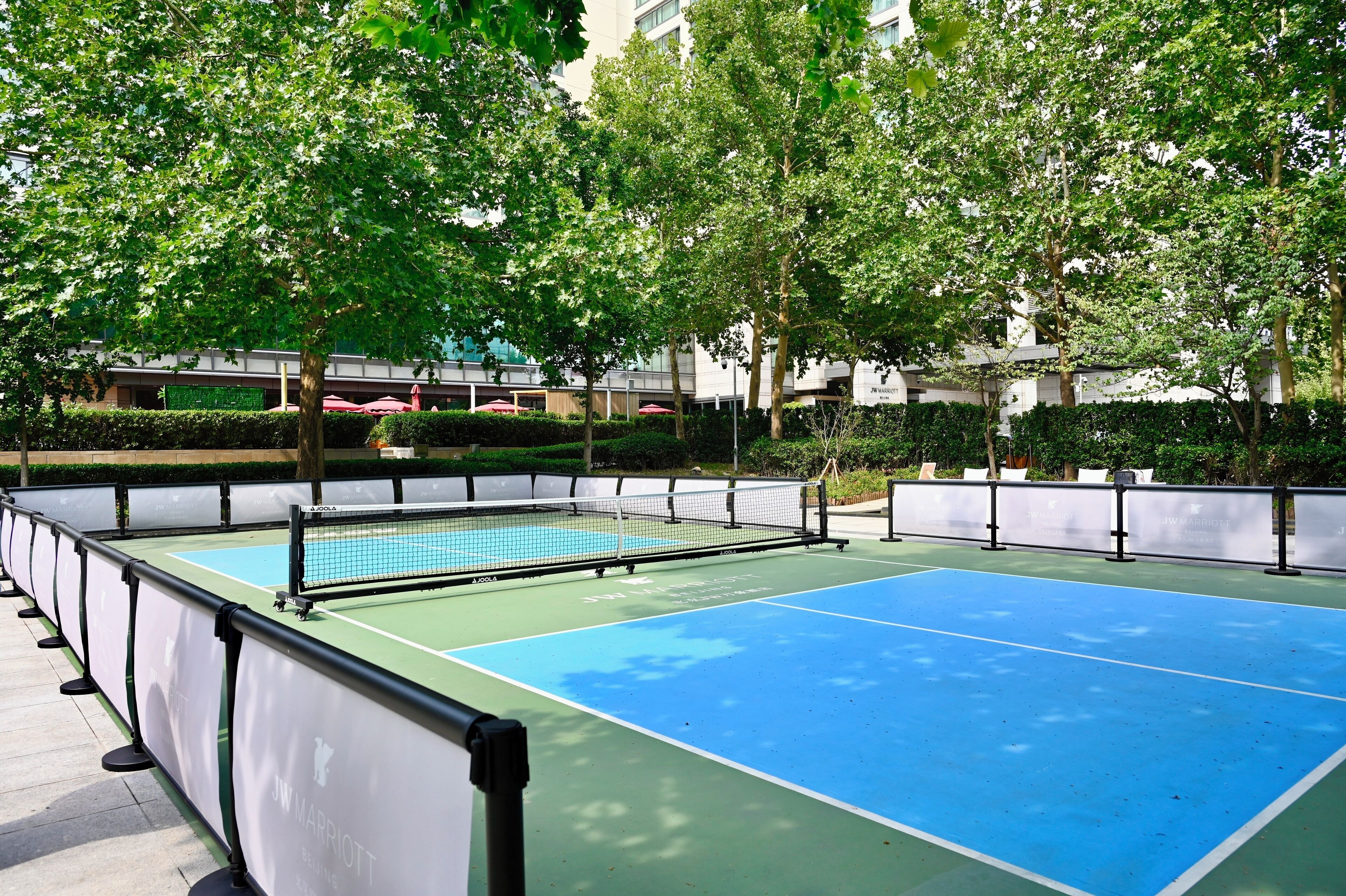 Ein Tennisplatz im Freien mit Netz, umgeben von Bäumen und einem Zaun.