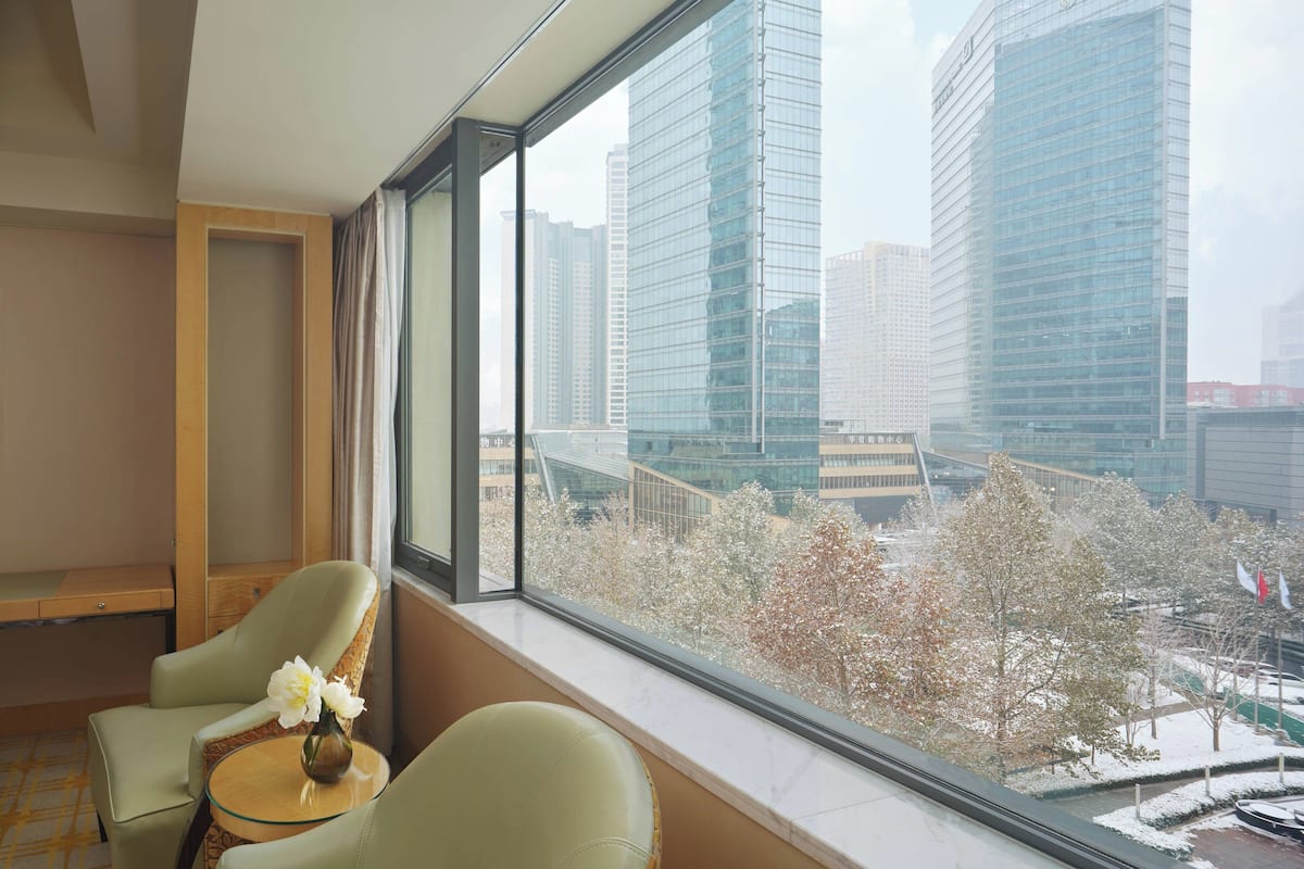 A hotel room with a large window offering a view of tall buildings and trees.