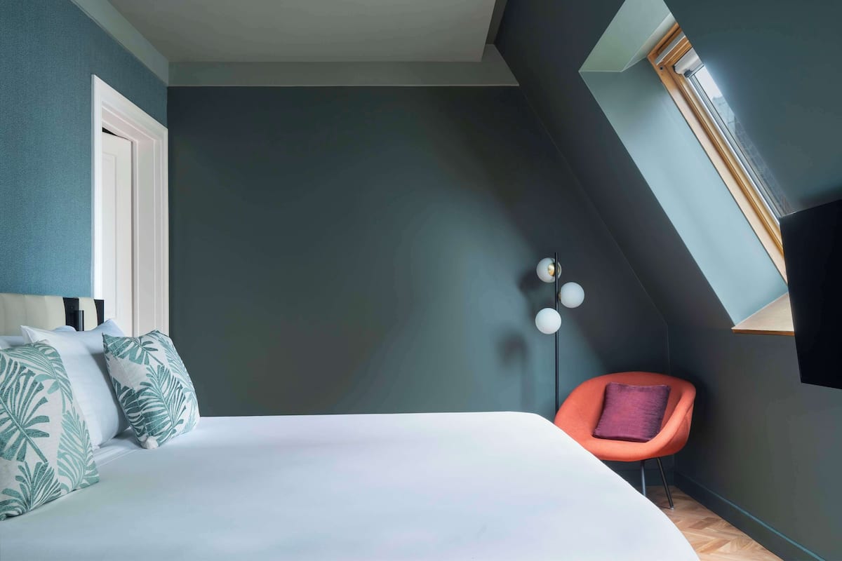 A bedroom with a bed, a chair, and a skylight.