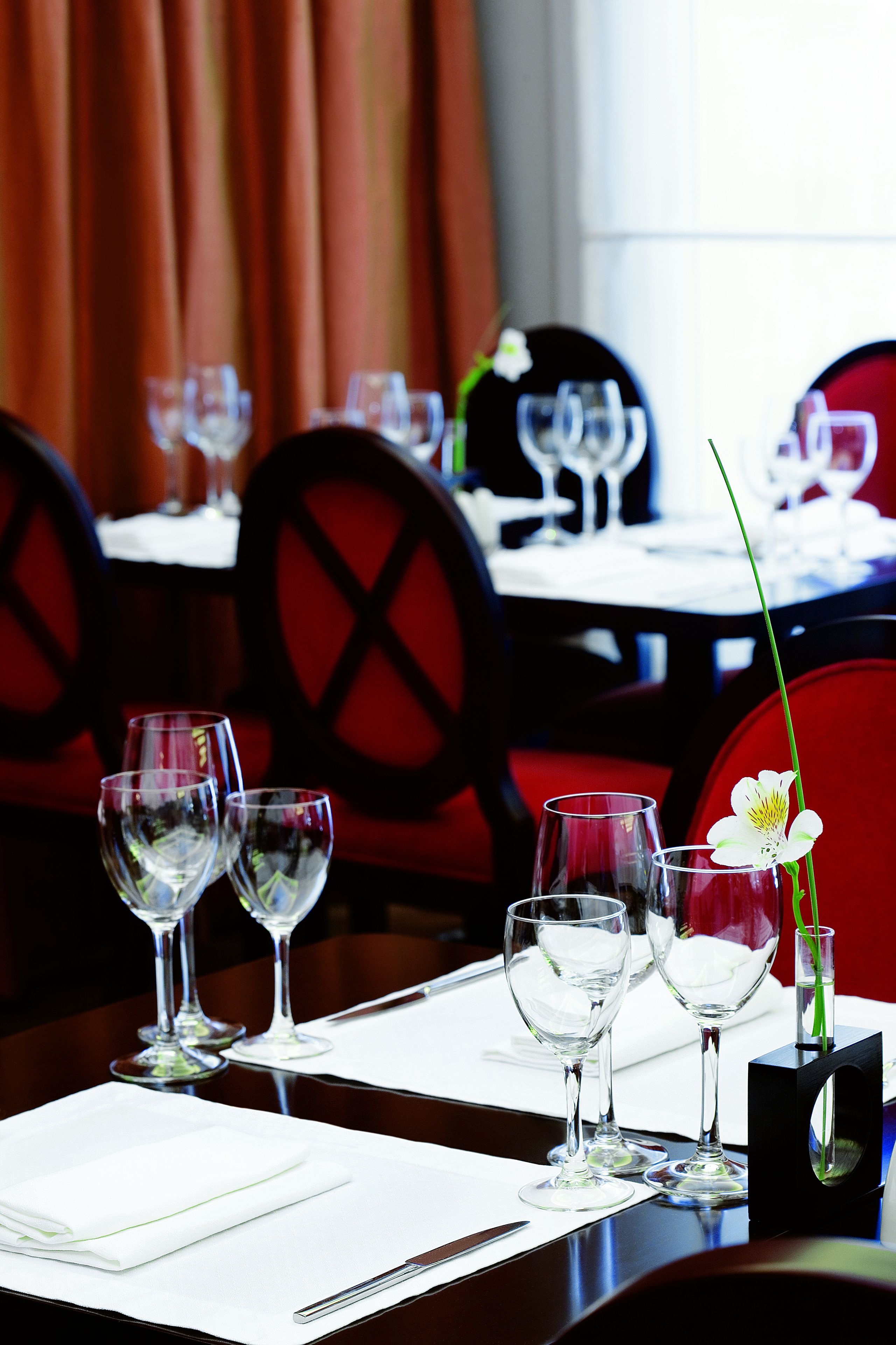 A dining table set with wine glasses, a vase with a flower, and a black napkin holder.