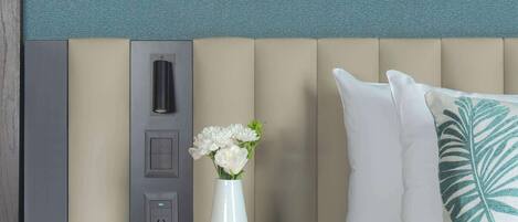 A neatly arranged hotel room with a bed, bedside table, and a wall-mounted control panel.