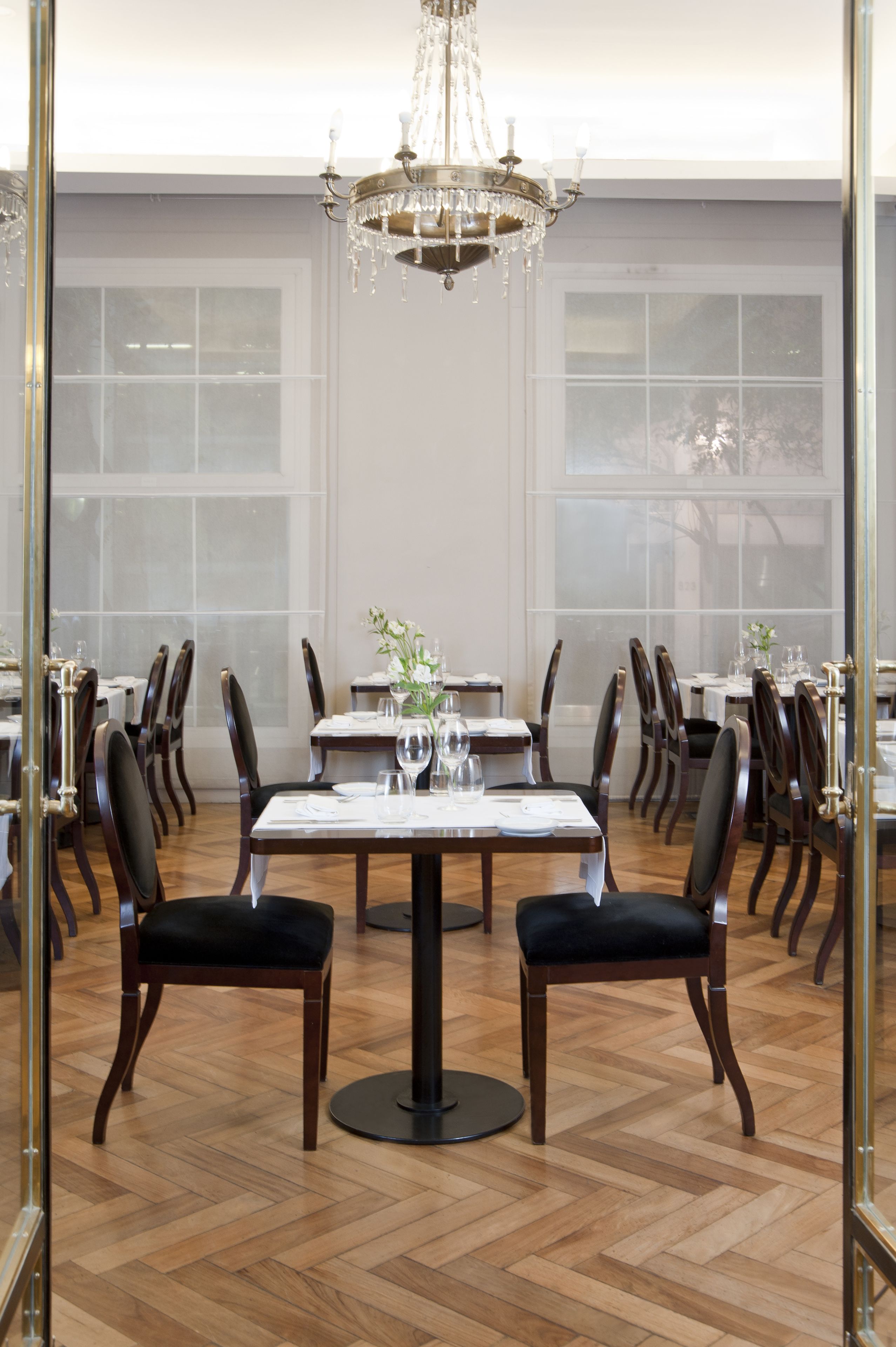 A dining area with a chandelier, wooden chairs, and tables set for a meal.