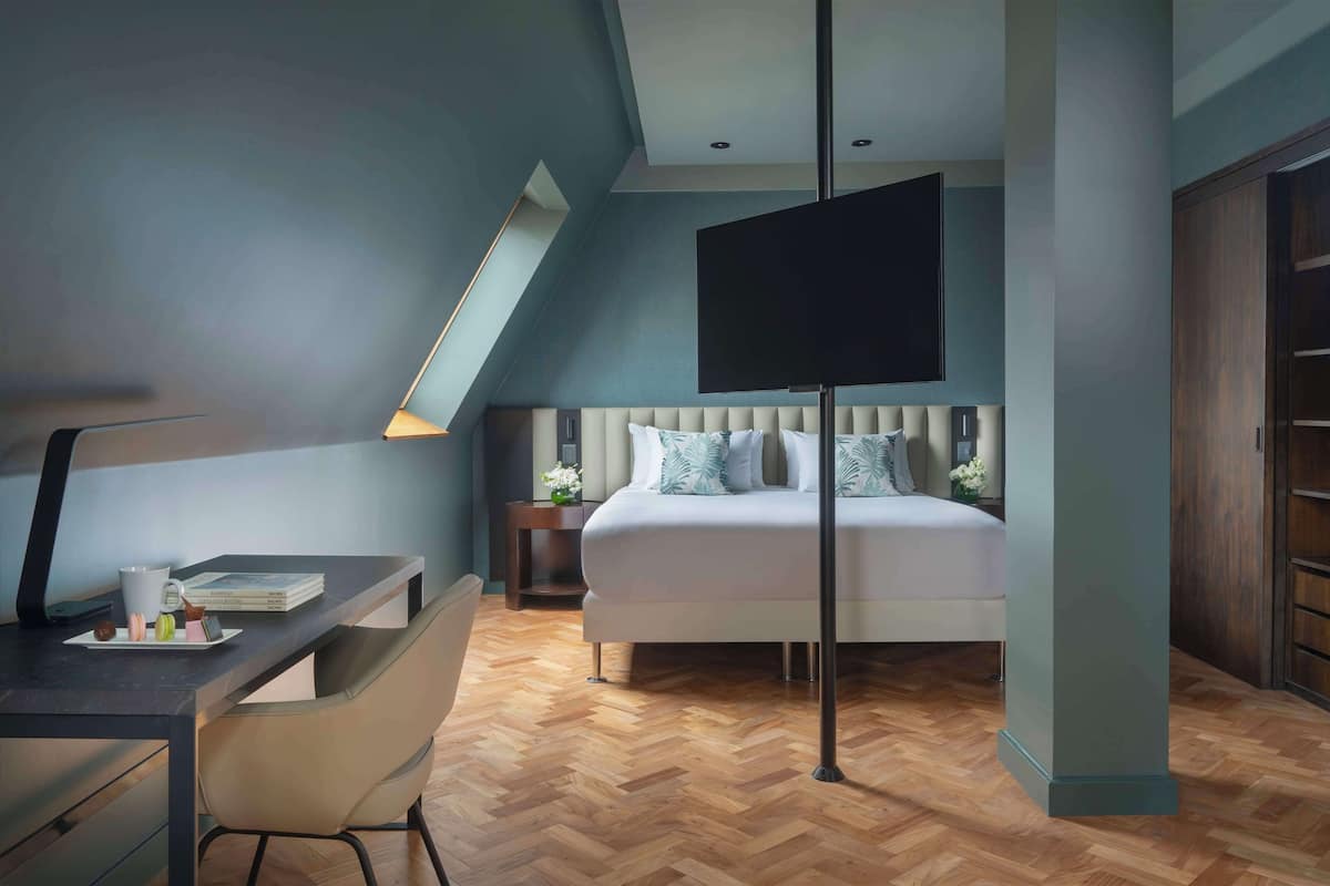 A modern bedroom with a bed, desk, chair, and a TV mounted on the wall.