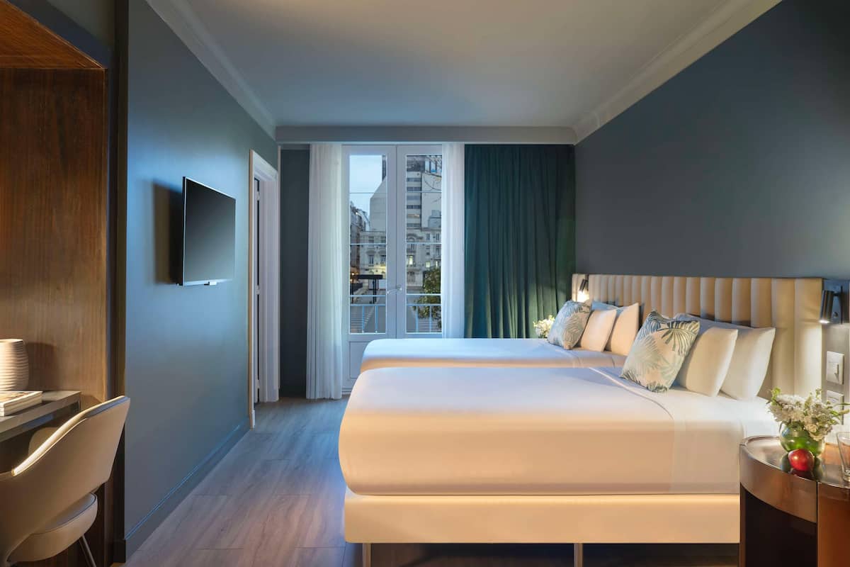 A hotel room with a bed, a TV, a desk, and a view of the city.