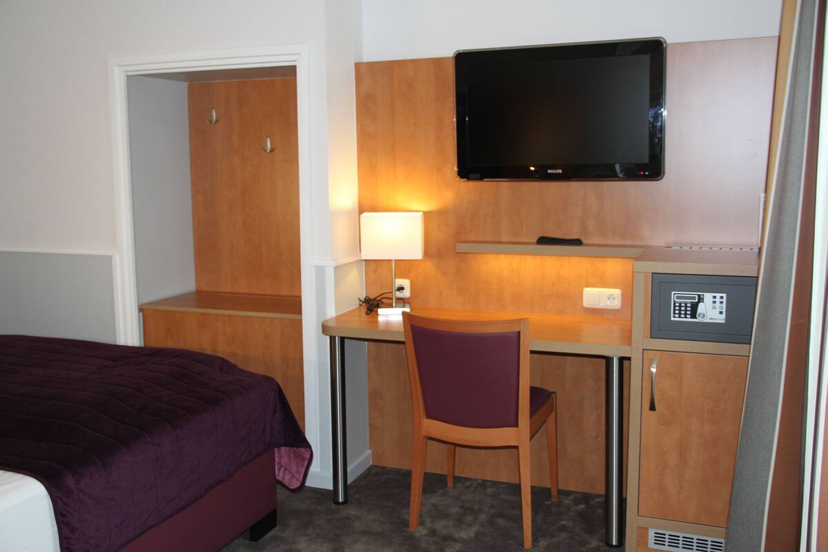 Ein Hotelzimmer mit einem Bett, einem Schreibtisch, einem Stuhl, einem Fernseher und einer Minibar.