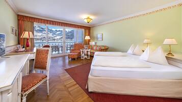 A hotel room with two beds, a desk, a chair, a small table, and a view of mountains through large windows.