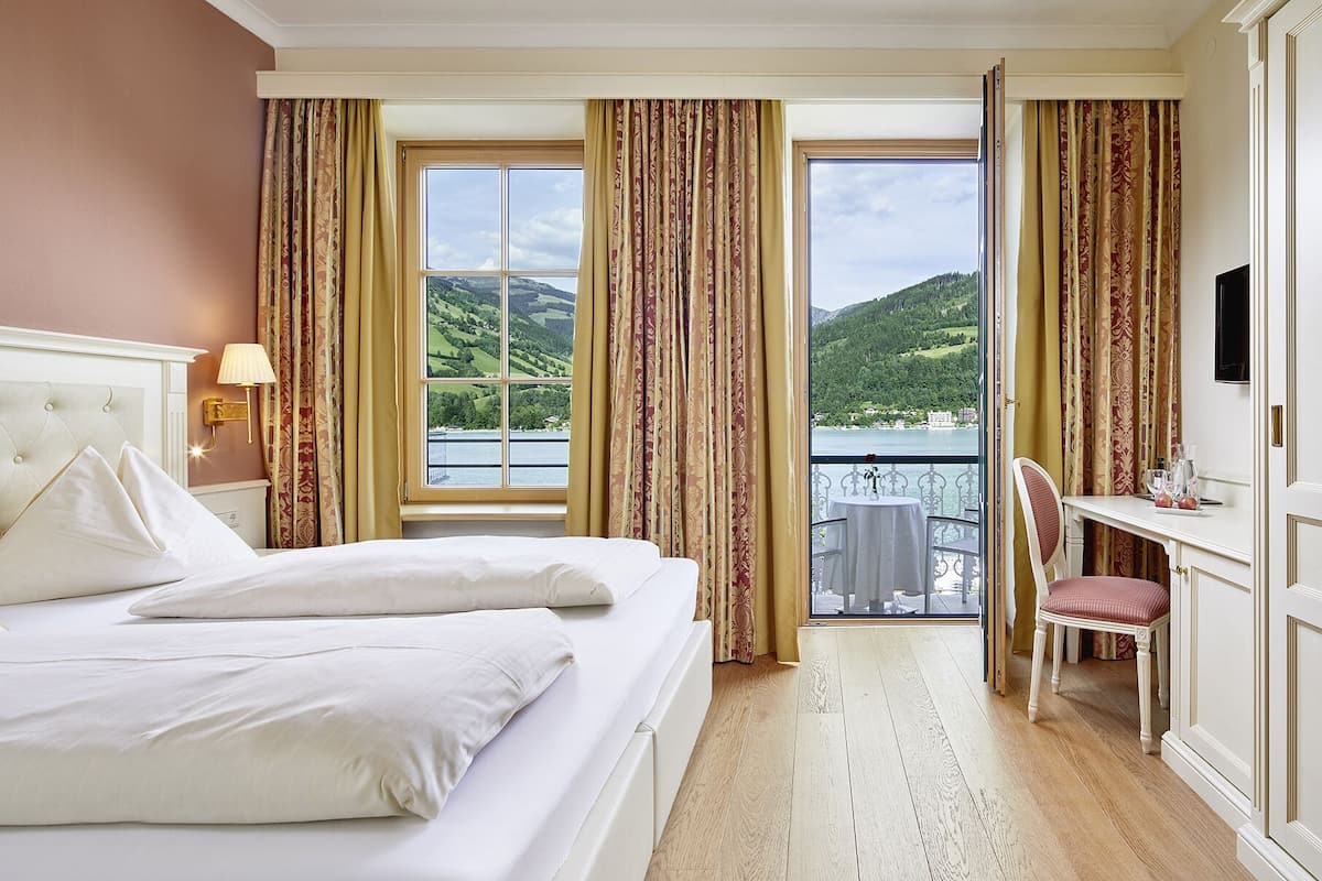 Ein Hotelzimmer mit Bett, Schreibtisch und Blick auf See und Hügel.
