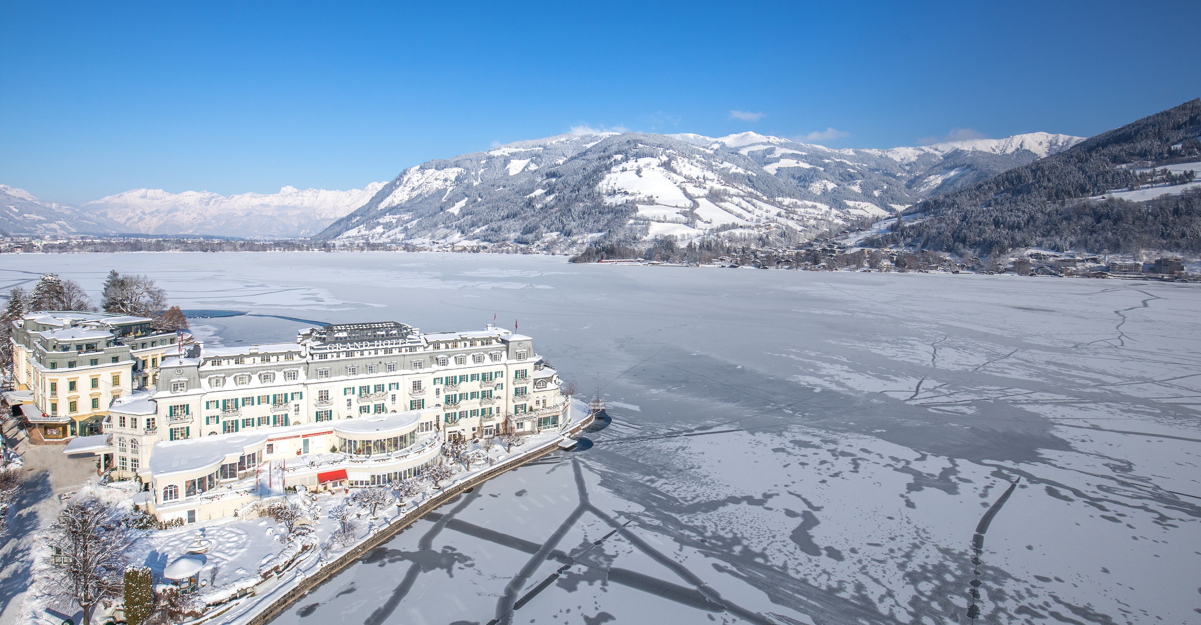A large hotel with multiple buildings, a waterfront, and snow-covered mountains in the background.