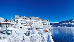Een statig hotel met een sneeuwbedekte tuin en uitzicht op een meer.