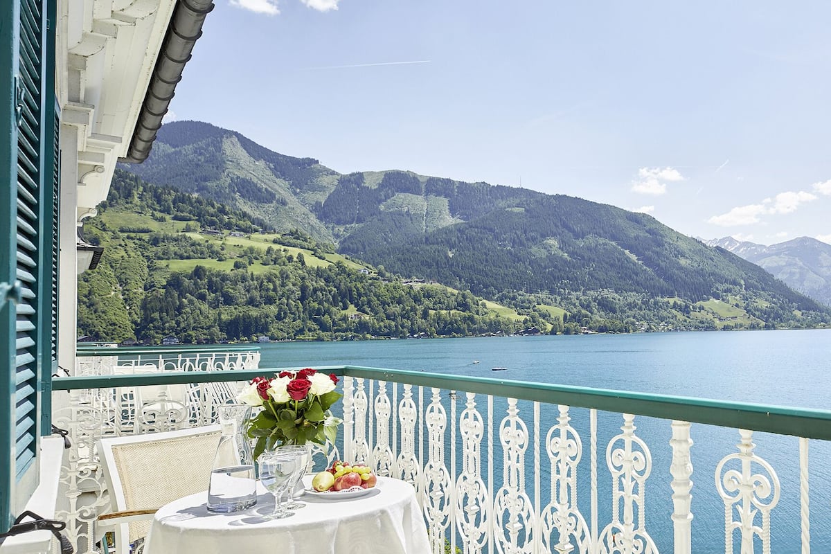 Un balcon avec une table dressée pour le dîner, donnant sur un lac et offrant une vue sur des montagnes en arrière-plan.