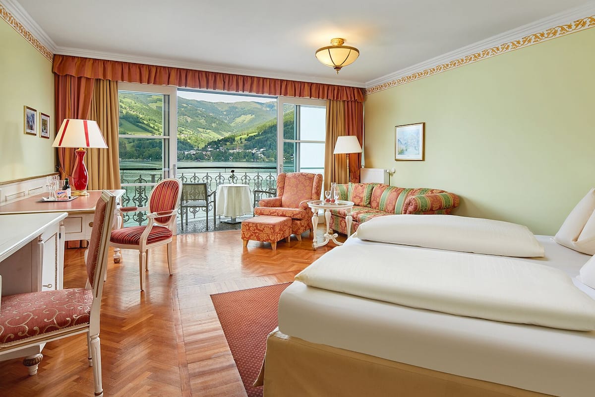 Une chambre d’hôtel avec un grand lit, un bureau, une chaise, un canapé et une vue sur un lac et des montagnes.