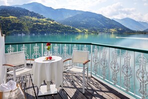 Une table entourée de chaises sur un balcon donnant sur un lac, avec des montagnes en arrière-plan.