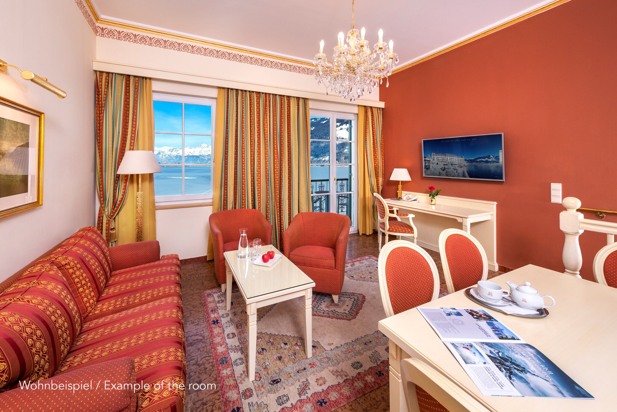 A hotel room with a sofa, chairs, a dining table, a chandelier, a window with curtains, and a painting on the wall.